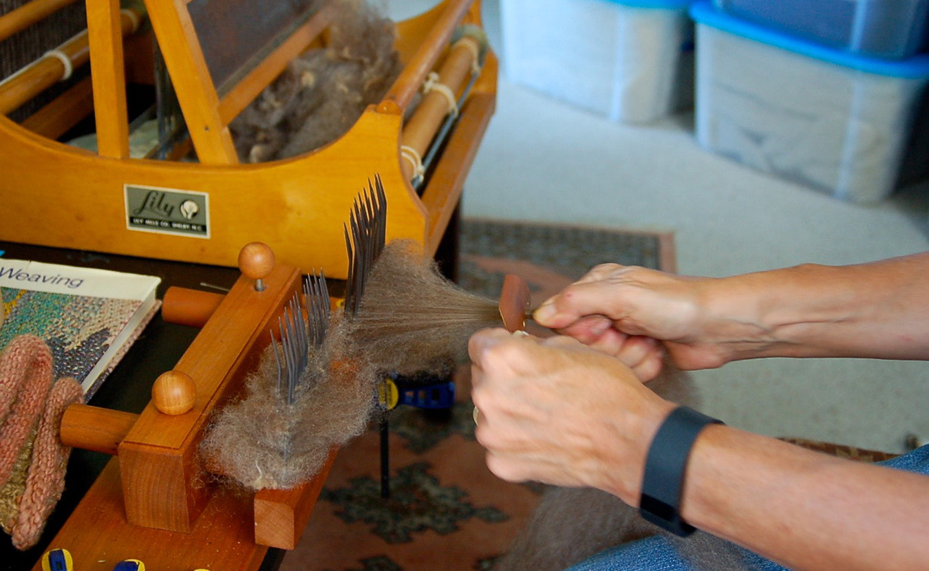 Whitney combs the fleece with sharp mettle tines to sift out debris and align the strands of fiber in a single direction. She then pulls the “combed top” through a small hole to create roving, which can then be spun into yarn. | Photo by Lindsay Welsch Sveen
