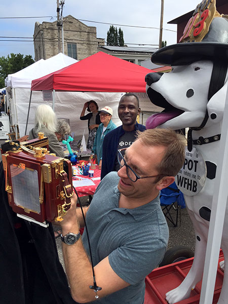 Photographer Adam Reynolds sets up a photo at the 4th Street Festival of the Arts and Crafts as Ron Bronson looks on from the WFHB table. | Limestone Post