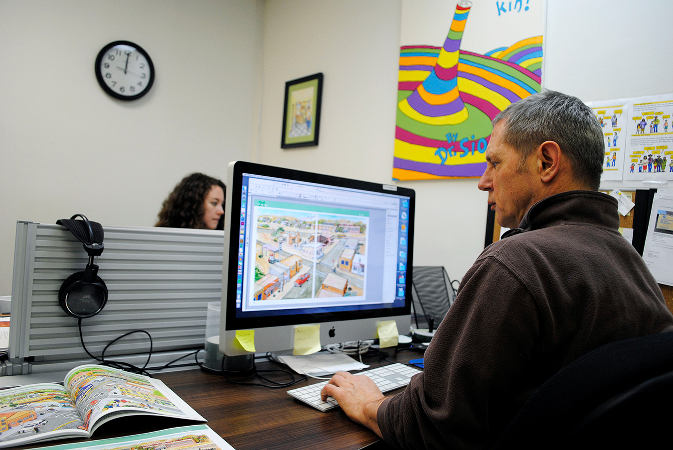 Publications Director Bob Rugh edits pages that will be featured in The Language Conservancy’s printed booklets. Graphic Designer Allison Horner works in the background. | Photo by Nicole McPheeters