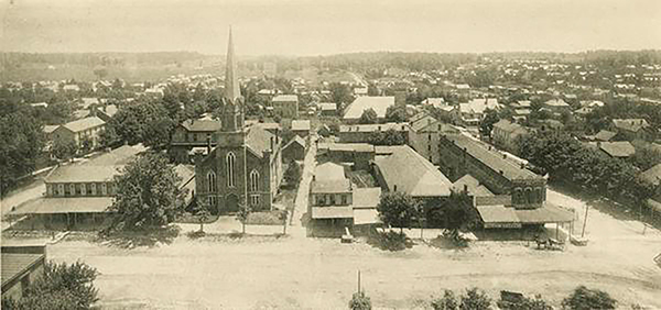 The east side of the downtown Square in 1891. The Indiana University Archives has labeled the buildings from left to right: "Faulkner House Hotel (at corner with covered sidewalk); meat market (behind tree); First Presbyterian Church; alley; bakery, barber shop; feed store ?; J. H. Kirby's Meat Market; grocery store (the tall white building behind the grocery store is the old National House Hotel at 113 thru 121 East Kirkwood. In later years this hotel became the Grundy Hotel and the Hotel Kirkwood)." | Photo courtesy of Indiana University Archives