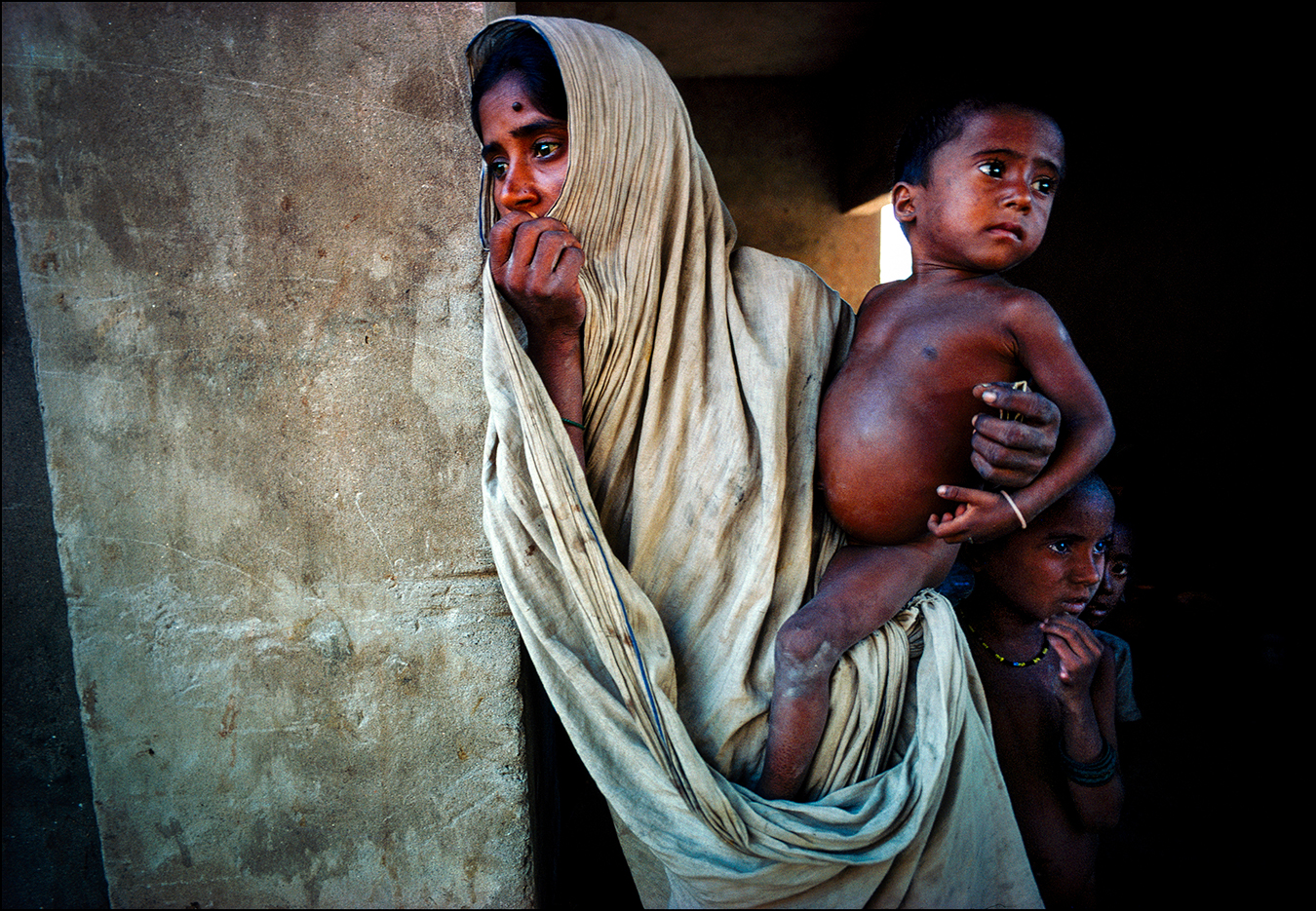 Ration card clutched in her left hand, a mother waits with her three hungry children for powdered milk donated by the United States and Canada and dispensed by the Dutch Red Cross — another mind-numbing scene in Bangladesh during the 1974 famine. International relief experts called Bangladesh the most underfed and overcrowded nation in the world, while The New York Times reported, "Mass hunger and starvation is no longer a threat. It is here." | © Steve Raymer / National Geographic Creative