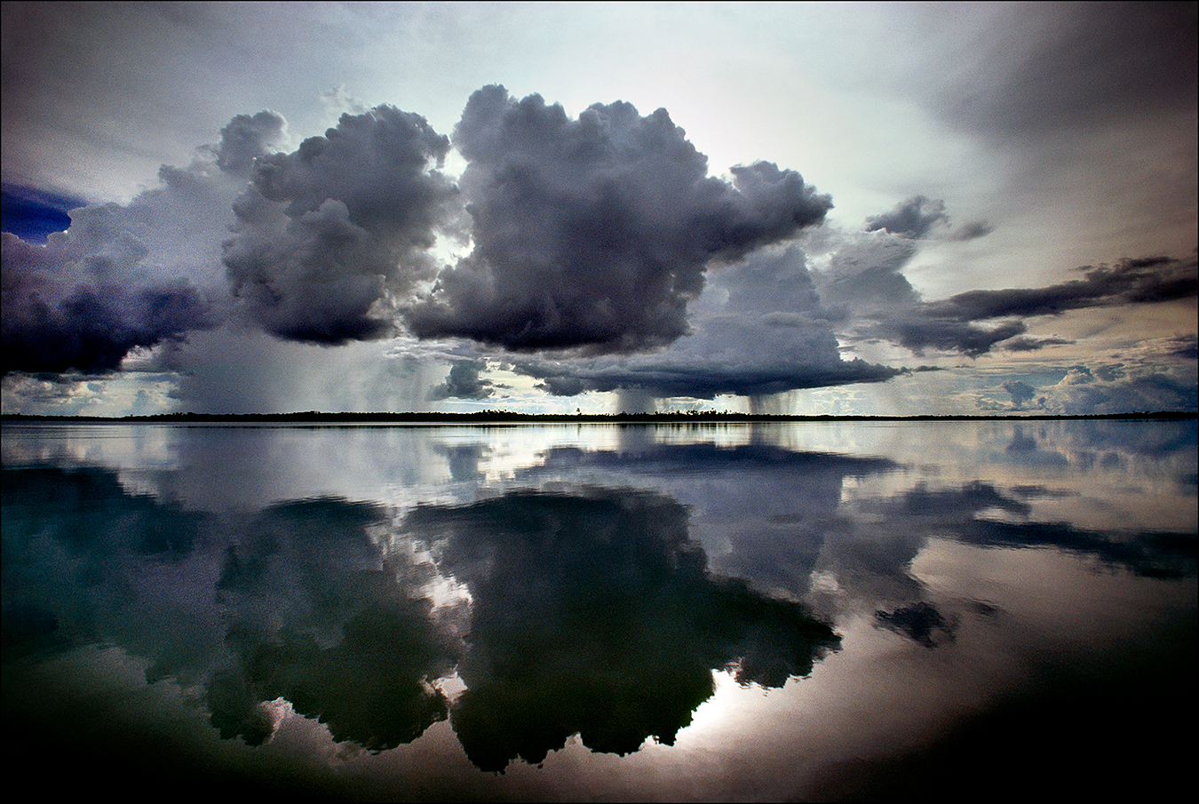 Menacing cumulus clouds are mirrored in the placid waters of Lake Murray, the largest lake in Papua New Guinea, covering an area of some seven hundred square miles. About five thousand indigenous communities inhabit this lake region. In 1923, The New York Times reported on an Australian expedition that used amphibious airplanes to chart Lake Murray and the explorers' close encounters with indigenous people called, at the time, "head-hunters." | © Steve Raymer / National Geographic Creative