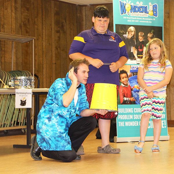 For many students in rural areas of Indiana, STEM learning fades as the school year ends, writes Patti Danner. But a variety of programs are bringing STEM access to rural areas. For example, pictured here is Bloomington's Wonderlab Museum Educator Nick Whites as he demonstrates sound principles with audience assistants Fred Harvey, left, and Esse Harvey during his June Symphony of Science outreach program in Shelburn. | Photo by Patti Danner