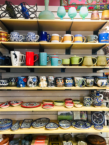 Global Gifts carries beautiful ceramics from all around the world. There are plenty of feline-themed options for the cat people in your life, kitchen and tableware for the gracious dinner hosts, a medley of mugs and pots for the coffee and tea drinkers, and even ceramic cell phone amplifiers for the podcast enthusiasts (yes, that’s a thing — can you spy the blue vessel that looks like it has a face?). Pottery from the West Bank, pictured on the lower two shelves, is always a favorite; the little bowls can be used to serve snacks and sauces or store jewelry and trinkets. The swirled Phoenician glass on the top shelf also hails from the West Bank — from Hebron Glass, a glass-blowing factory that has been in business since 1890.